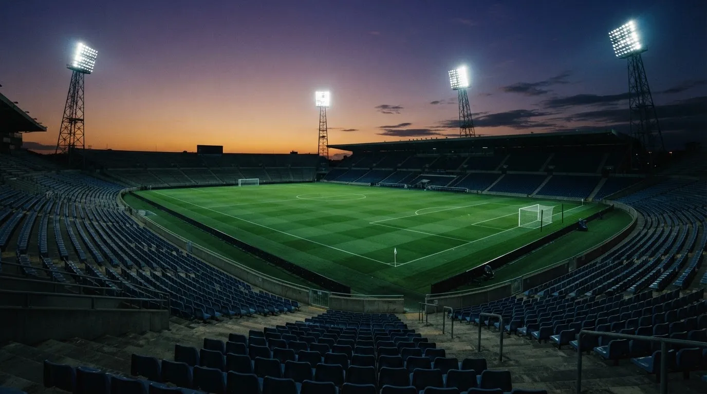 An empty football stadium with floodlight masts at dusk