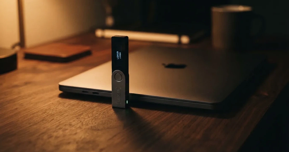 A hardware wallet and a closed laptop on a desk in dim light